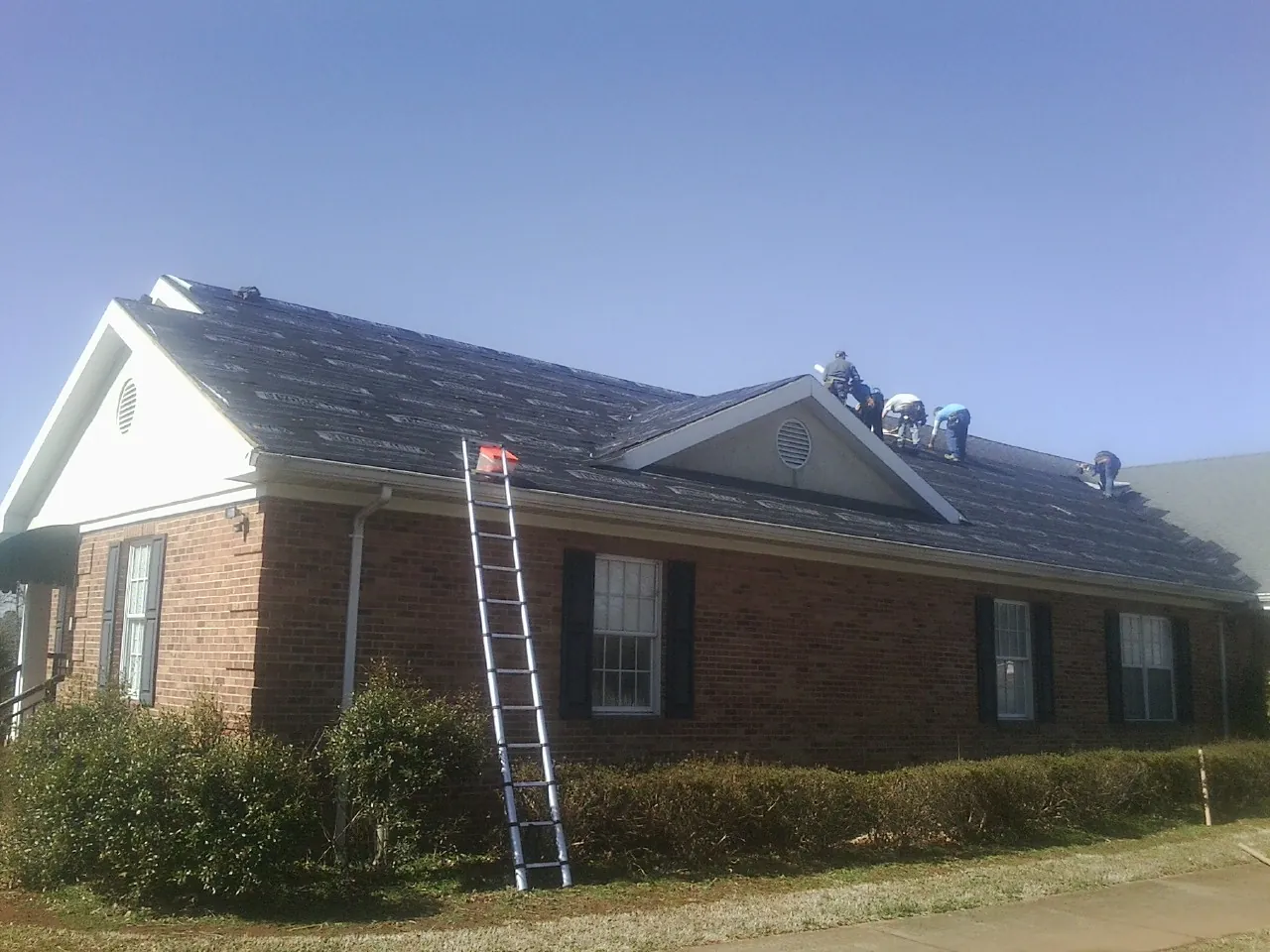 Crew tearing shingles off a brick ranch roof with a ladder set — Metal Roof Repair work by our crew in Enumclaw