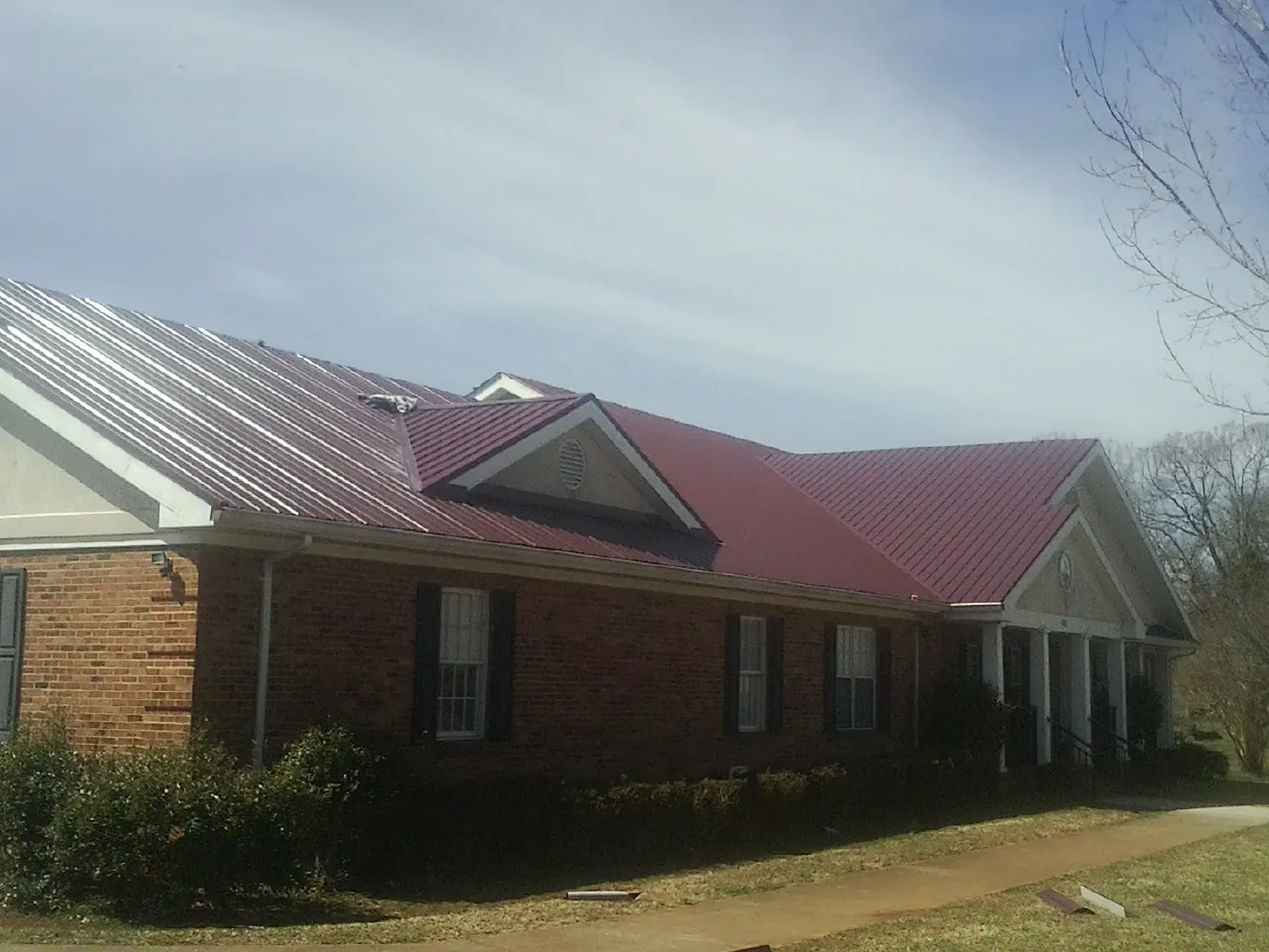Red metal roof with gabled entries on a long brick building, from a Hail Damage Roof Repair job in Enumclaw