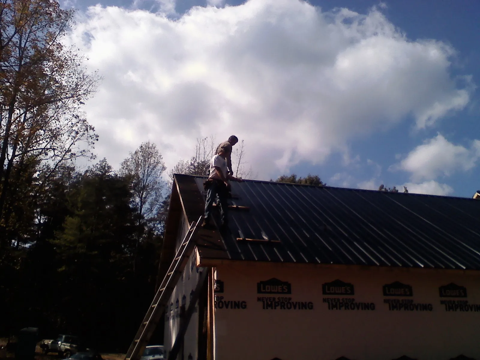 Roofer fastening dark metal panels high against a cloudy sky, from a Roof Inspection job in Enumclaw