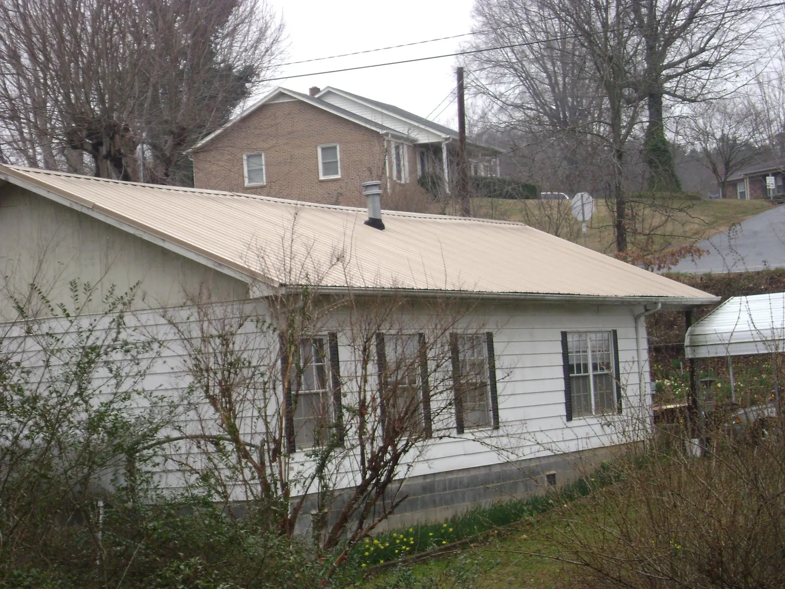 Tan metal roof on a white sided house set into a hillside — Commercial Roofing by Roofing Brothers in Enumclaw